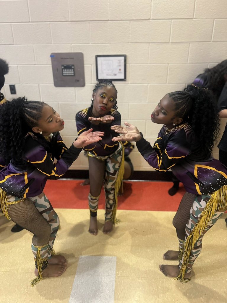 Three dancers from Royal Family of Peoria IL make kissy faces at each other behind the scenes of the majorette dance competition